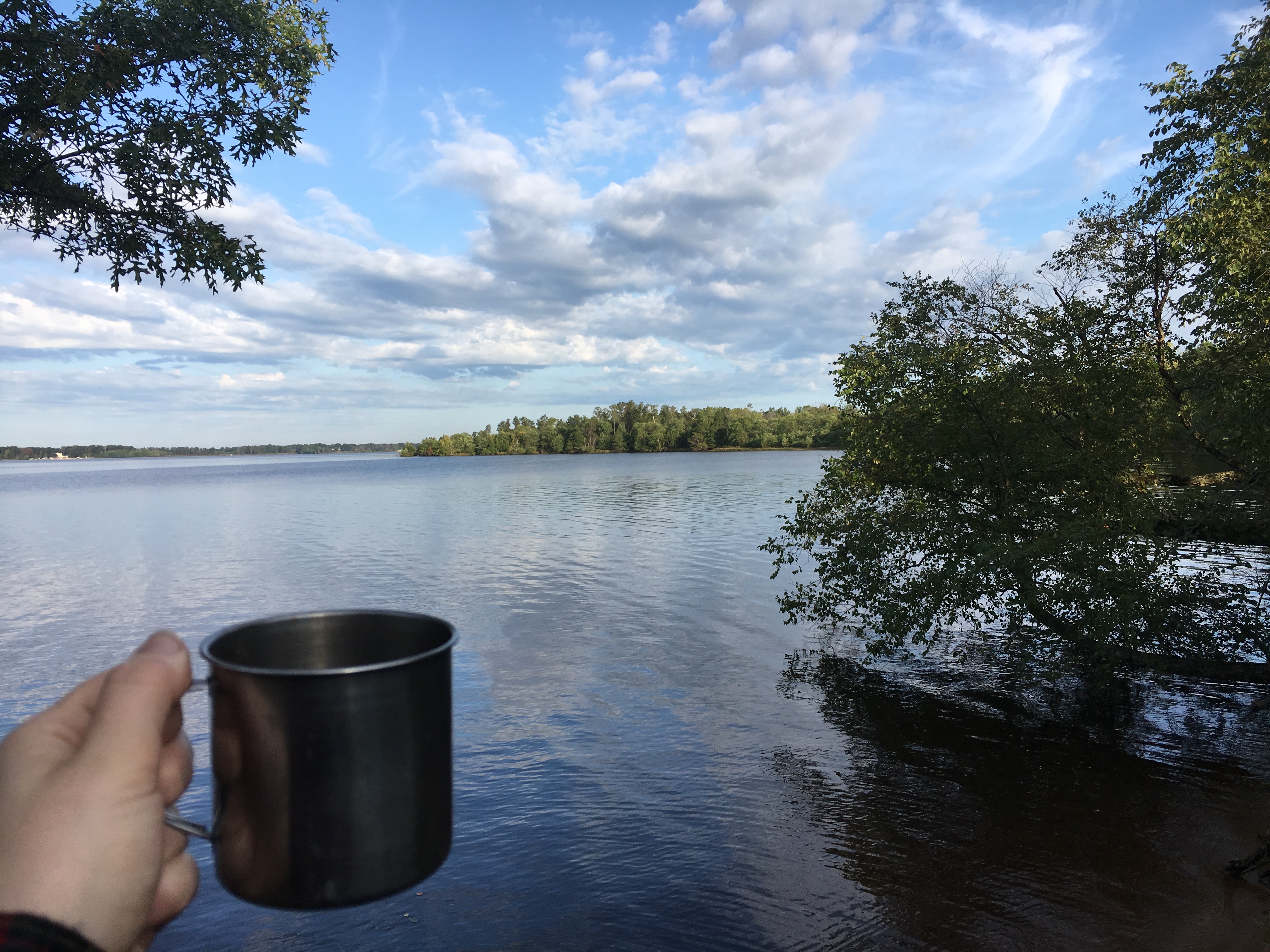 A cup of coffee held in front of a scenic image of the river. 